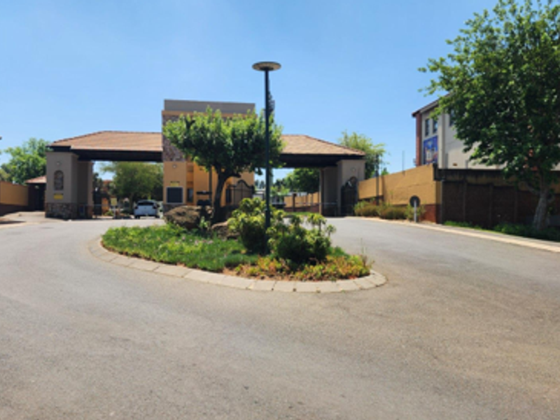 The entrance to the apartment complex features a secure gatehouse, paved driveway, and landscaped traffic island.