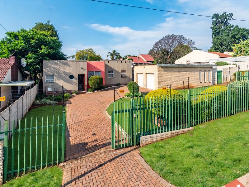 Front view of a residential property featuring a paved driveway, double garage, and secure metal perimeter fencing with an electric gate.