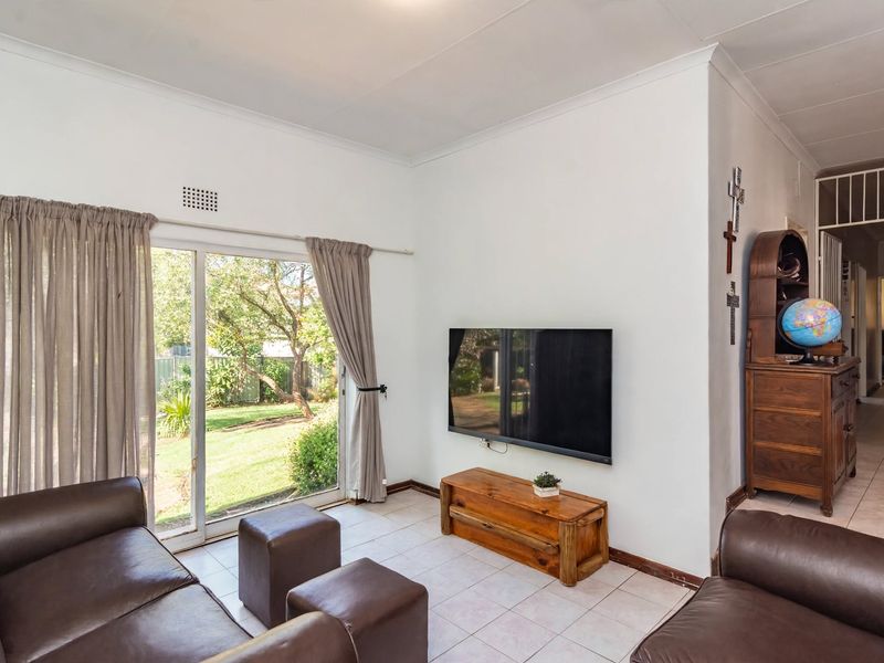 A bright living room featuring ceramic floor tiles, a coved ceiling, and a large sliding glass door providing direct access to the rear garden.