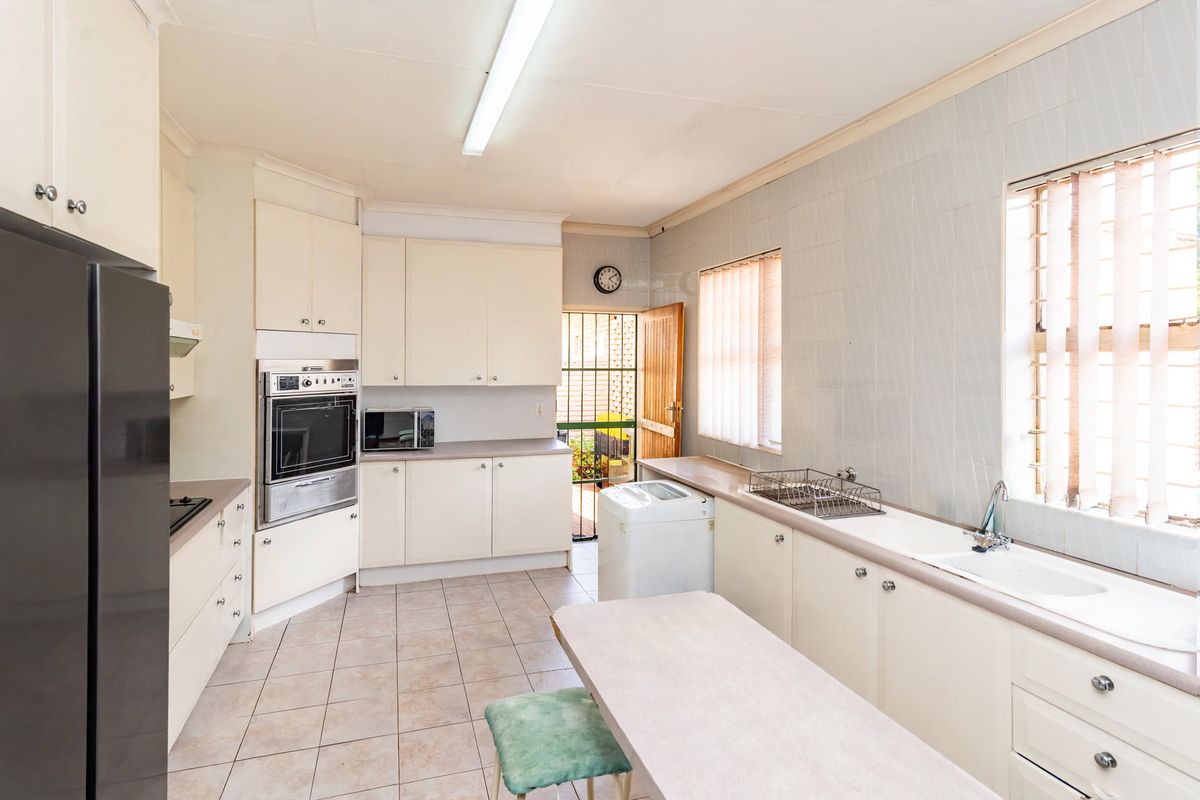 Functional kitchen featuring built-in cabinetry, integrated oven, tiled splashbacks, and direct access to the exterior via a security gate.