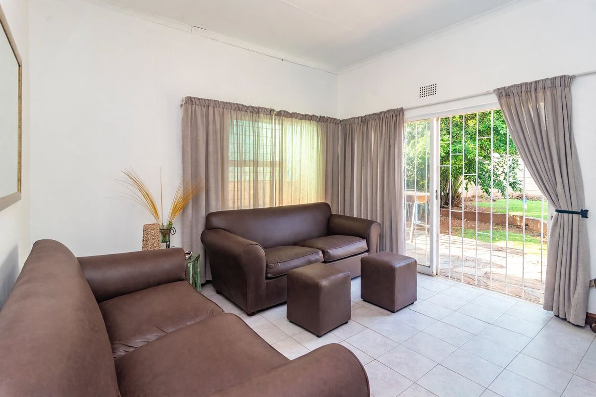 A living room featuring tiled flooring and a sliding glass door with security gate, providing direct access to the garden area.