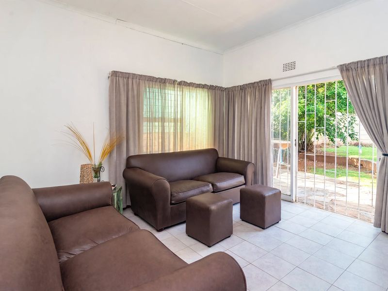 A living room featuring tiled flooring and a sliding glass door with security gate, providing direct access to the garden area.