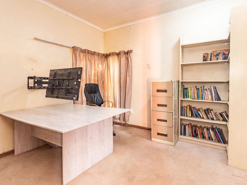 A home office space featuring a wall-mounted monitor arm and built-in shelving, requiring cosmetic updates to the walls and flooring.