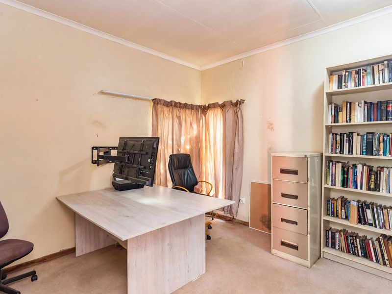 A home office space featuring carpet flooring and wall-mounted monitor hardware, currently requiring cosmetic updates and wall repairs.