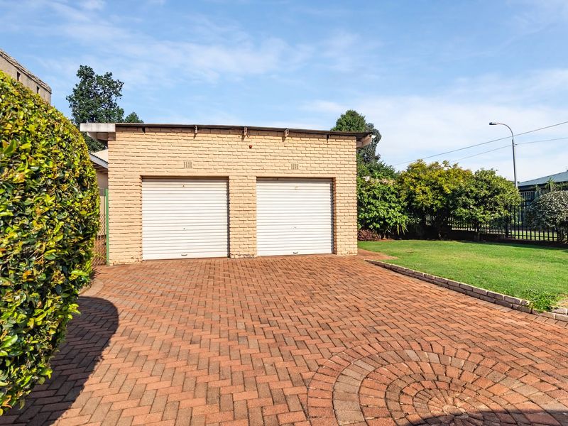 A detached double garage featuring a brick exterior, roll-up doors, and a well-maintained paved driveway set within a landscaped garden.