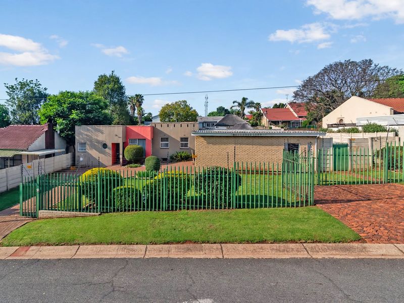 Front view of a residential property featuring a paved driveway, manicured lawn, and secure metal perimeter fencing with integrated electric security wires.