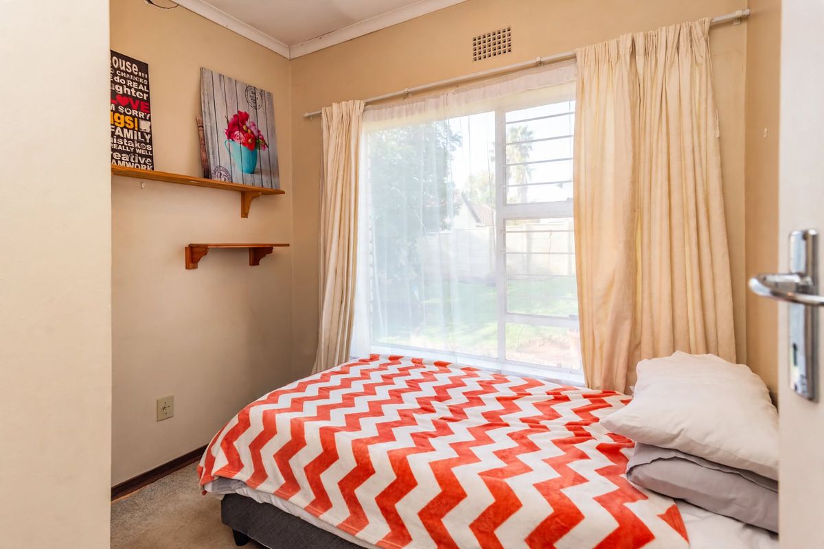 A standard bedroom featuring a window with security bars, wall-mounted shelving, and neutral wall finishes.