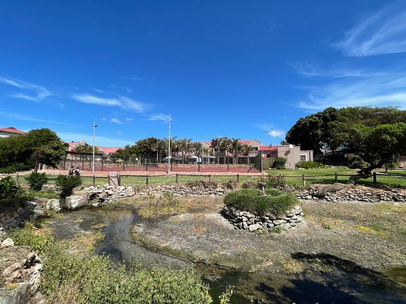 A view of a communal tennis court facility set within a landscaped garden area with stone retaining walls and a water feature.