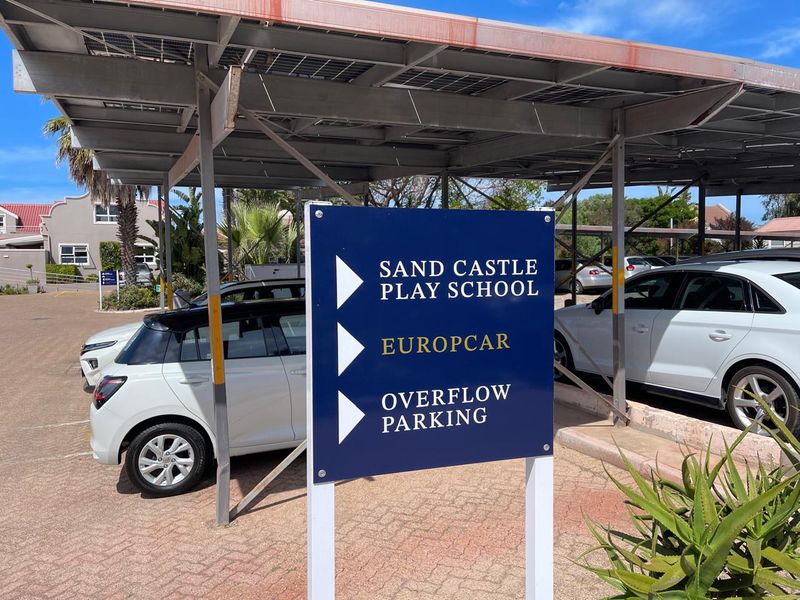 A paved parking area featuring a solar panel carport structure and directional signage for local facilities.