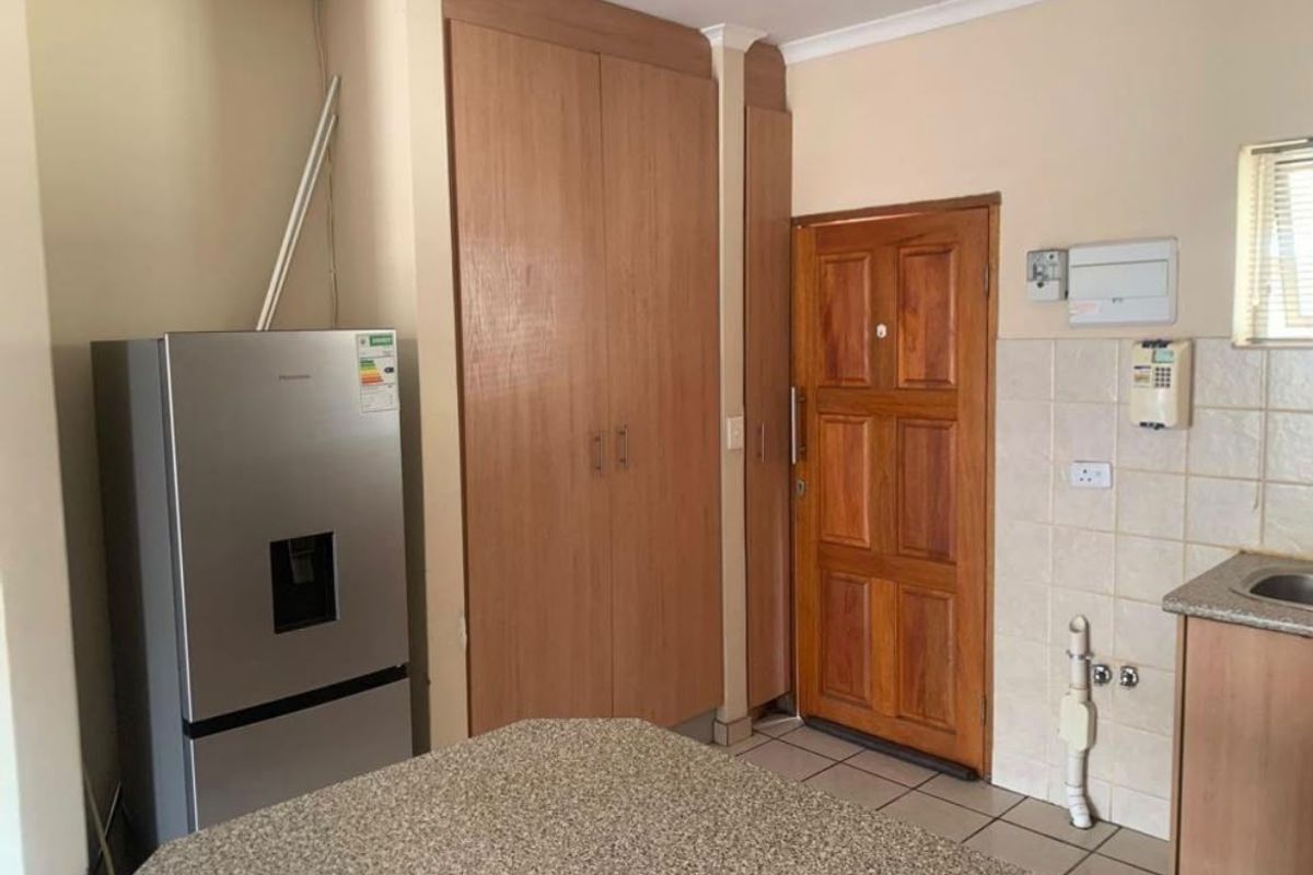 A functional kitchen area featuring built-in wooden cabinetry, granite countertops, and tiled flooring, with direct access to an exterior wooden door.