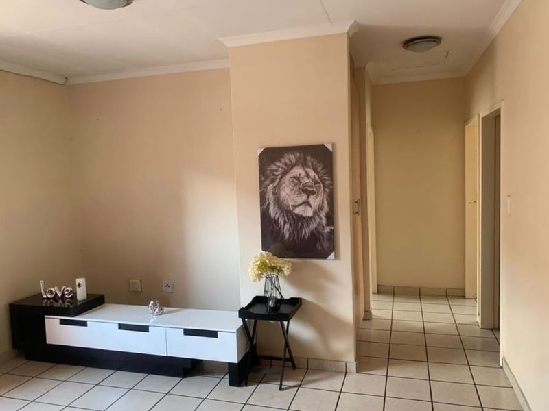 A neutral-toned living area featuring tiled flooring and a central pillar, leading into a hallway with access to other rooms.