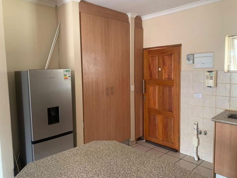 A functional kitchen area featuring built-in wooden cabinetry, granite countertops, and tiled flooring, with direct access to an exterior wooden door.