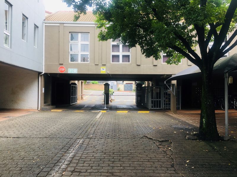 Front entrance view of the apartment complex featuring a paved driveway, security boom gate access, and covered parking area.