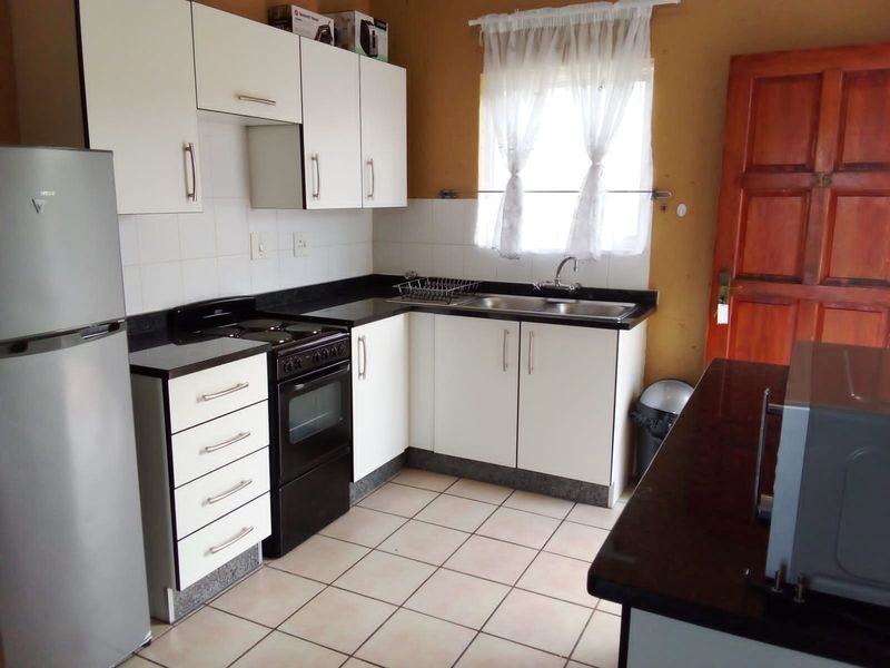A functional kitchen featuring white cabinetry, dark countertops, tiled flooring, and a freestanding stove, offering a practical layout for daily meal preparation.