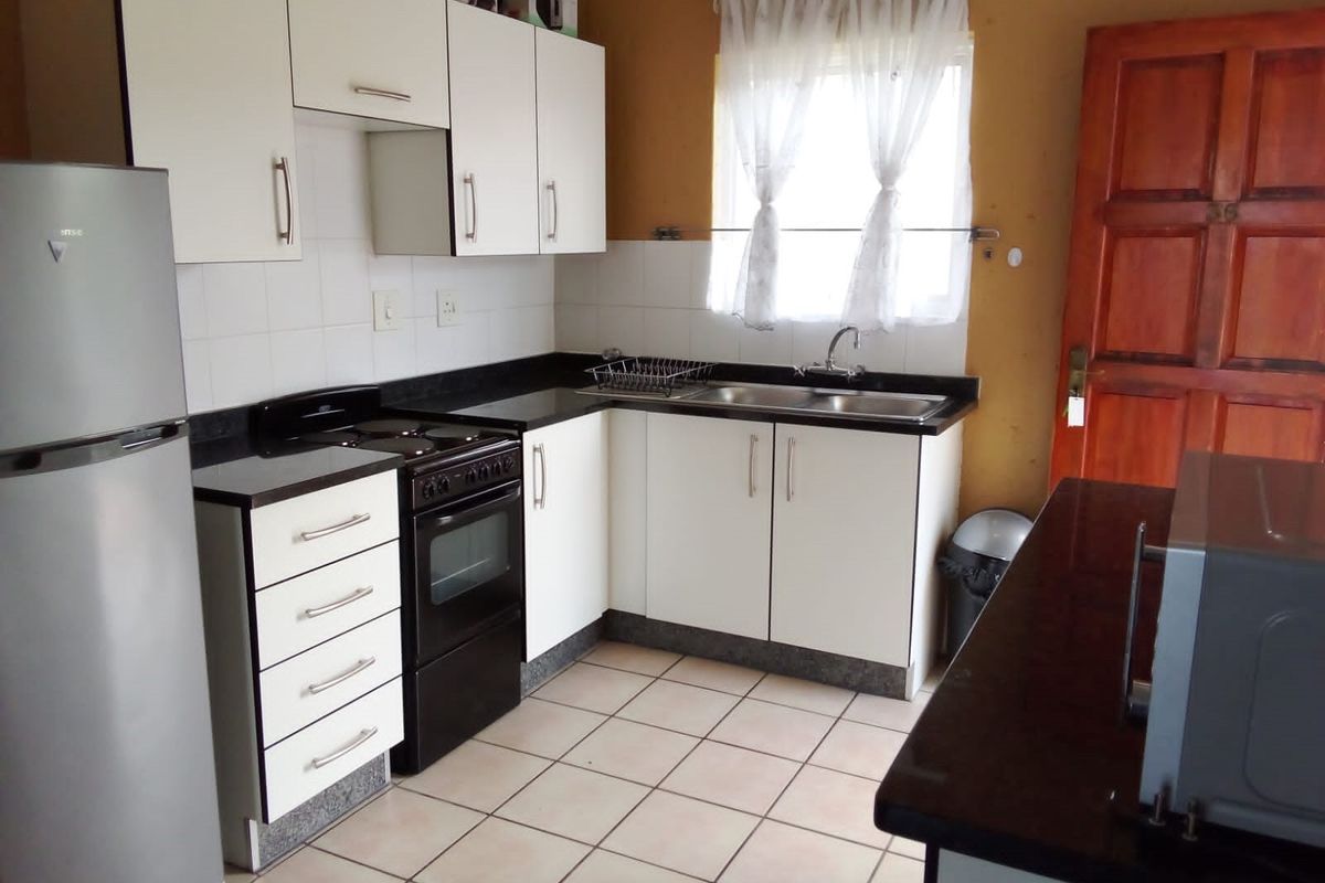 A functional kitchen featuring white cabinetry, dark countertops, tiled flooring, and a freestanding stove, offering a practical layout for daily meal preparation.