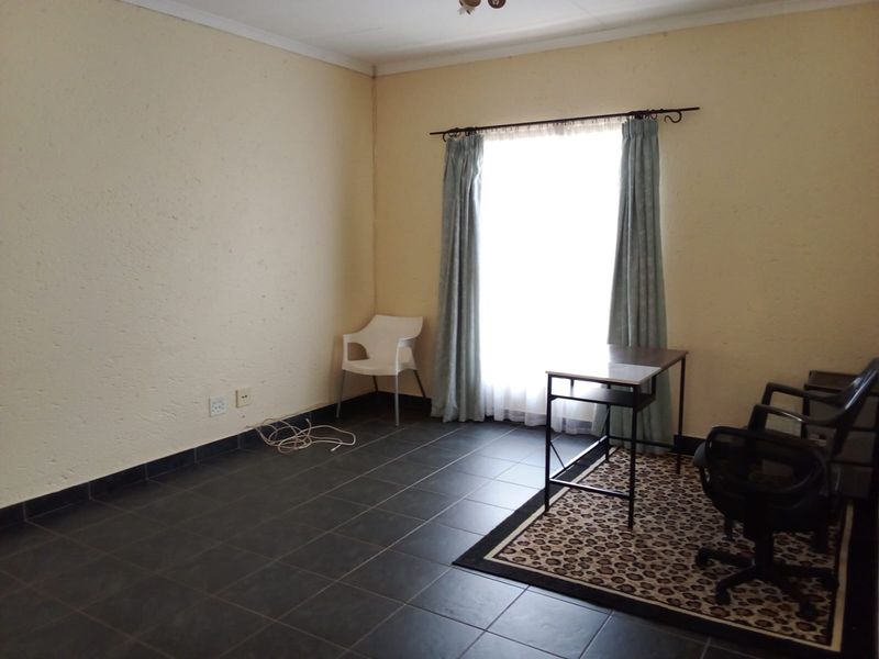 A living area featuring dark tiled flooring and a large window with curtain fittings, providing a neutral space ready for personalization.