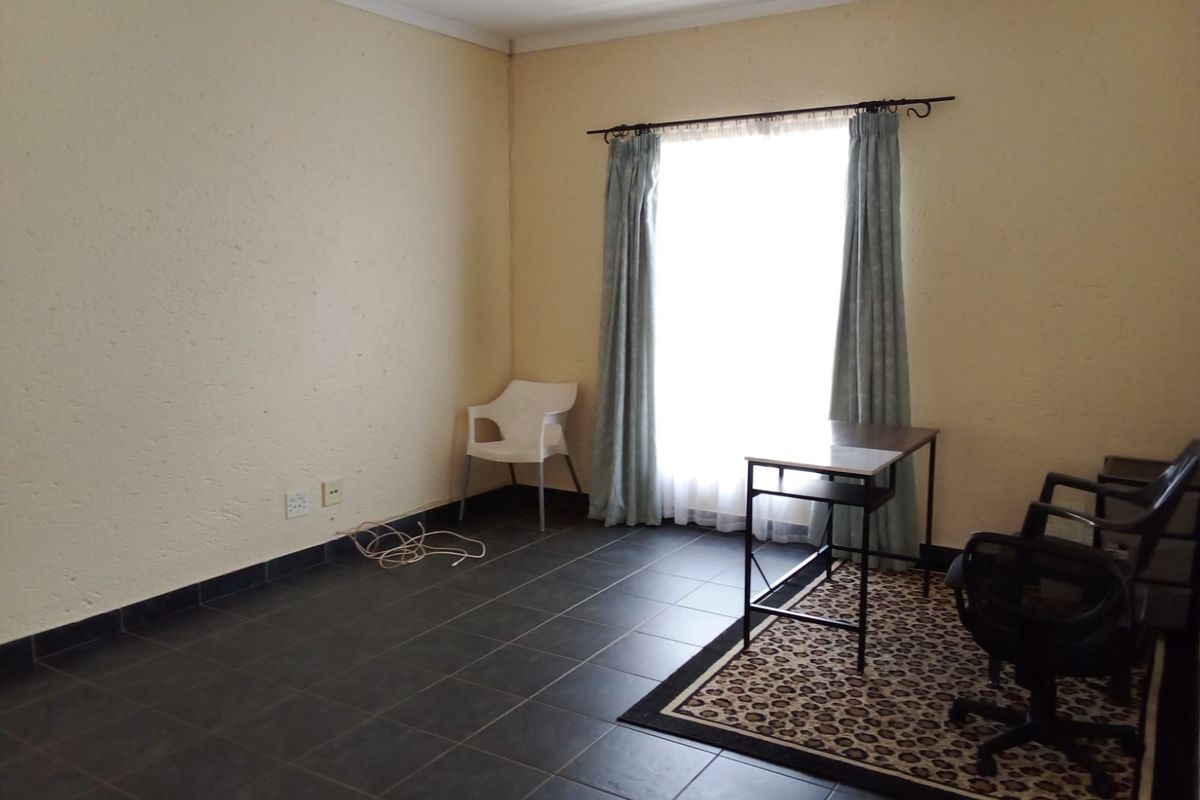 A living area featuring dark tiled flooring and a large window with curtain fittings, providing a neutral space ready for personalization.