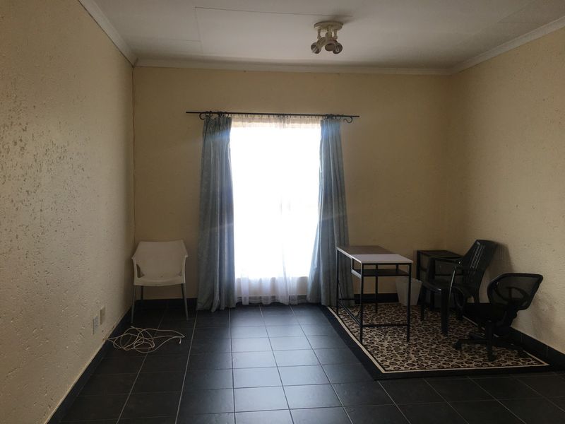 A bedroom featuring dark tiled flooring, a central ceiling light, and a window with a curtain rod, presenting a blank canvas for potential updates.