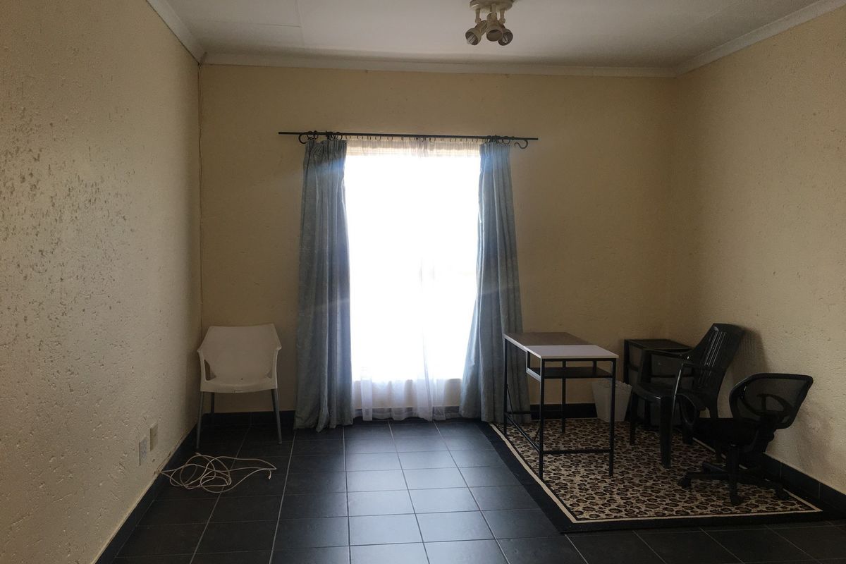 A bedroom featuring dark tiled flooring, a central ceiling light, and a window with a curtain rod, presenting a blank canvas for potential updates.