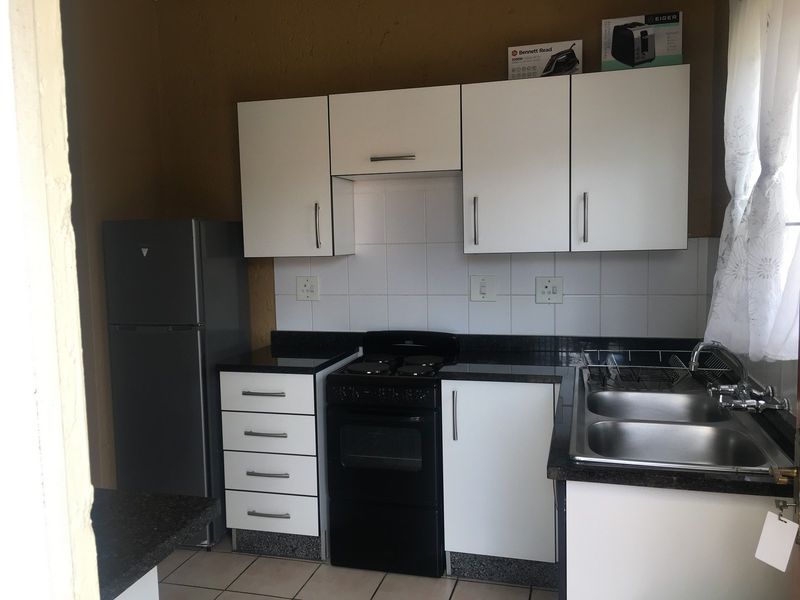 Compact kitchen featuring white cabinetry, black granite countertops, tiled backsplash, and a freestanding oven with a double bowl stainless steel sink.