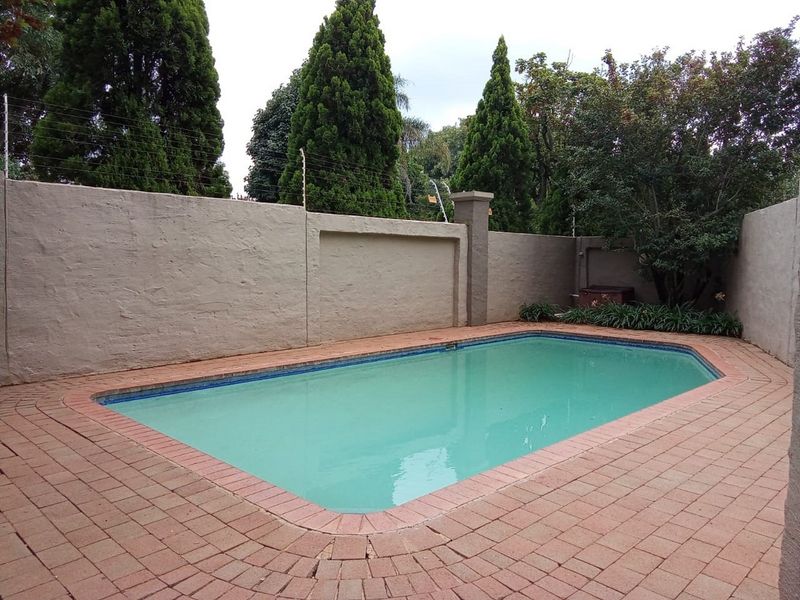 A private outdoor swimming pool area featuring brick paving, enclosed by a high perimeter wall with integrated electric fencing for added security.
