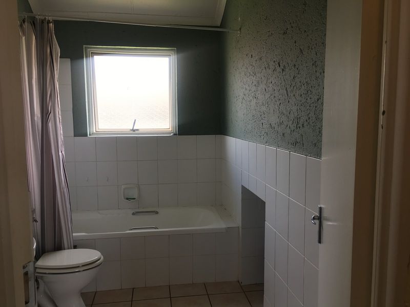 A functional bathroom featuring a built-in bathtub, toilet, and tiled finishes, offering a blank canvas for modern renovation and aesthetic updates.