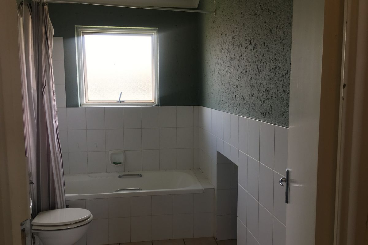 A functional bathroom featuring a built-in bathtub, toilet, and tiled finishes, offering a blank canvas for modern renovation and aesthetic updates.