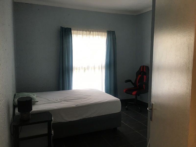 A bedroom featuring dark tiled flooring and a window with curtains, requiring cosmetic updates to the wall finishes.