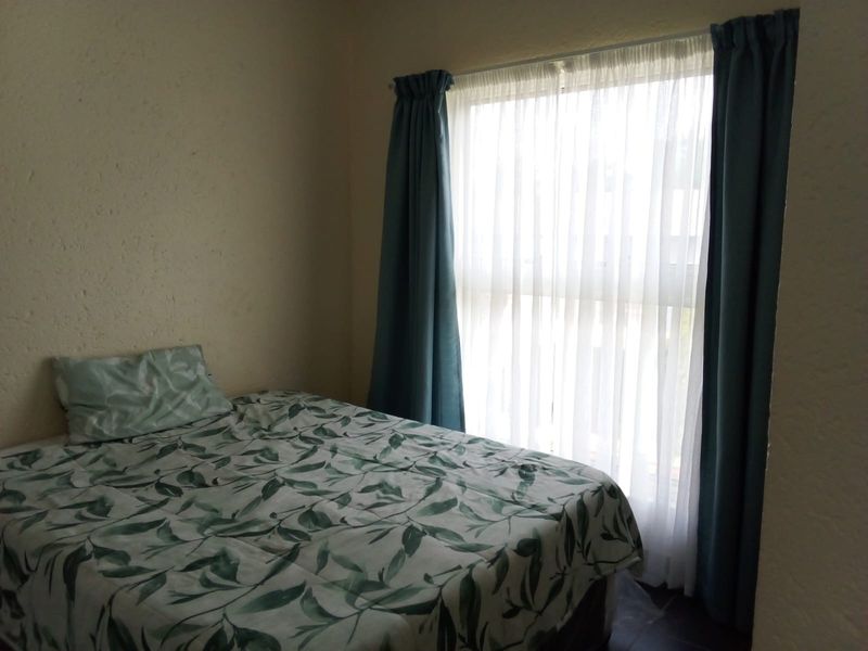 A simple bedroom featuring a window with installed curtain tracks, providing natural light and a neutral backdrop for potential interior design updates.