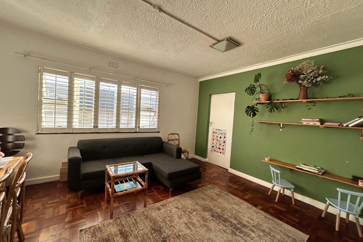 A living room featuring original parquet flooring, window shutters, and a feature wall with built-in shelving.