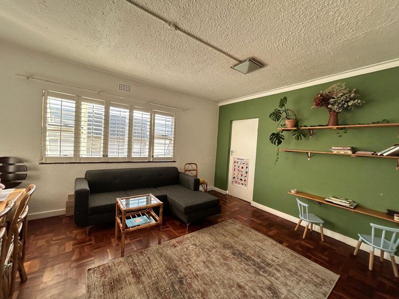 A living room featuring original parquet flooring, window shutters, and a feature wall with built-in shelving.