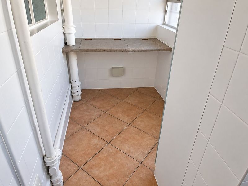 A clean, functional laundry or utility area featuring tiled walls, tiled flooring, and a built-in stone countertop with exposed plumbing infrastructure.