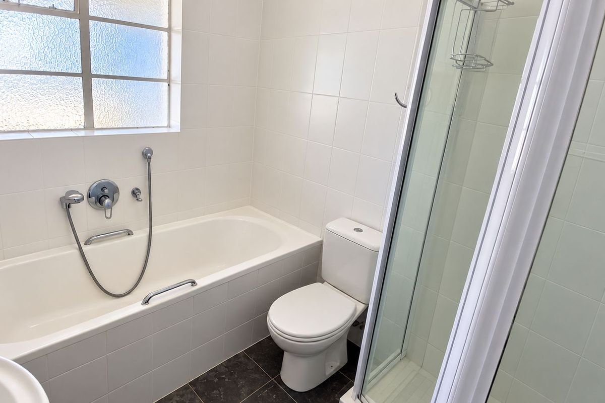A clean, functional bathroom featuring a bathtub, separate shower enclosure, and toilet with neutral wall tiling and dark floor tiles.