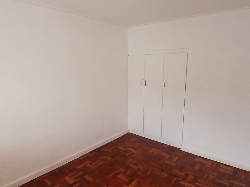A clean, empty bedroom featuring classic parquet flooring and white built-in cupboards, offering a neutral canvas for personalization.
