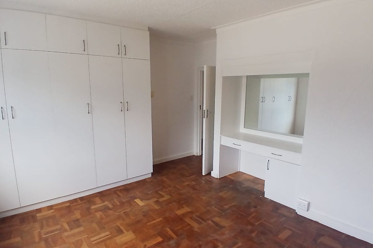 A spacious bedroom featuring classic parquet flooring, extensive built-in cupboard storage, and a dedicated built-in vanity area with a mirror.