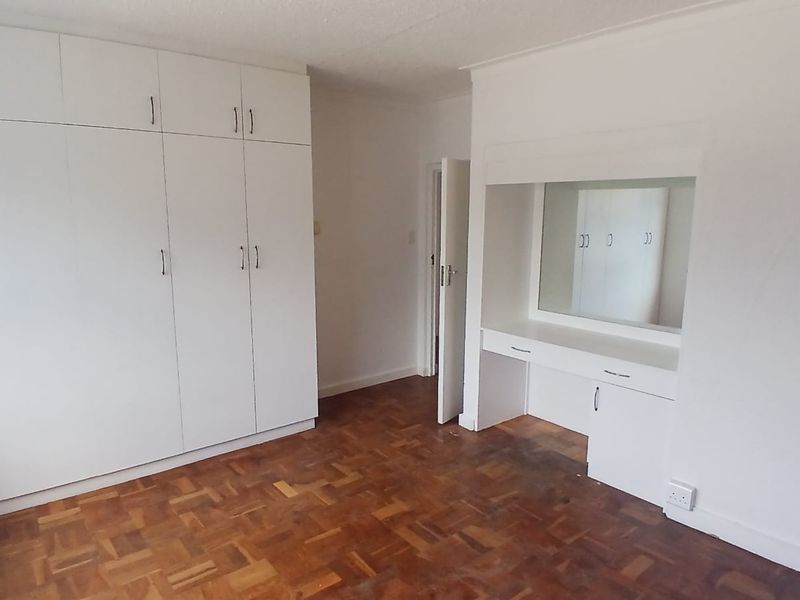 A spacious bedroom featuring classic parquet flooring, extensive built-in cupboard storage, and a dedicated built-in vanity area with a mirror.