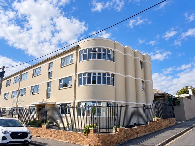 A well-maintained apartment building featuring a distinctive curved facade, multi-pane windows, and secure perimeter fencing with a brick boundary wall.