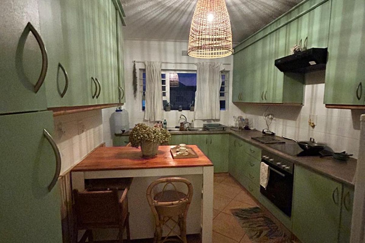A functional kitchen featuring green cabinetry, built-in oven and hob, tiled flooring, and a central breakfast nook area.