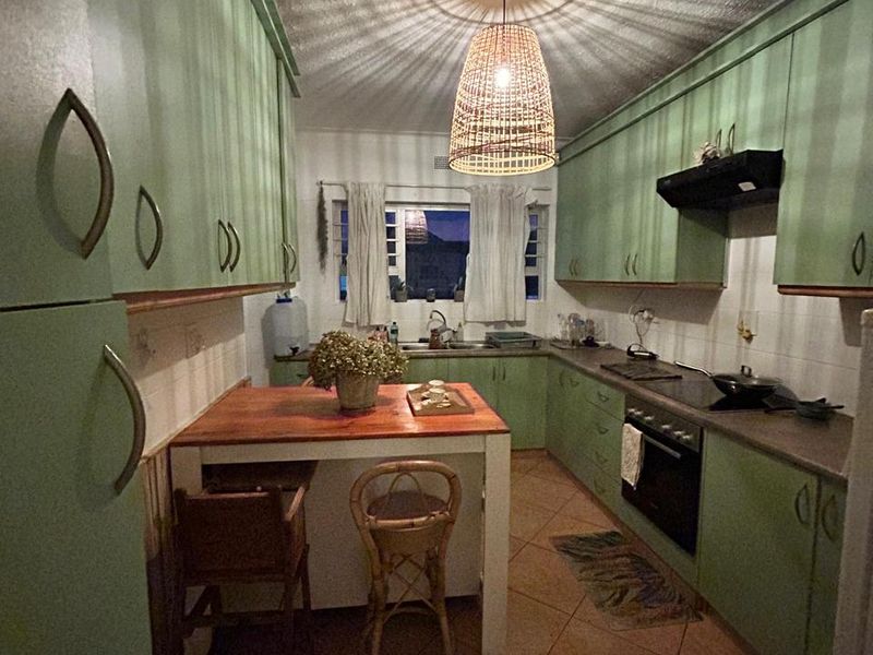 A functional kitchen featuring green cabinetry, built-in oven and hob, tiled flooring, and a central breakfast nook area.