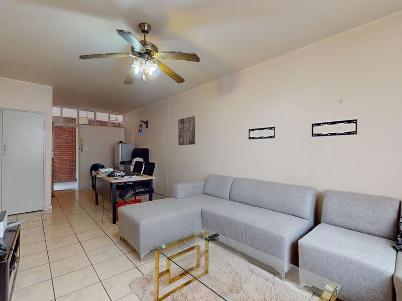 A living room featuring tiled flooring, a ceiling fan, and neutral wall finishes, providing a functional space with potential for modern updates.