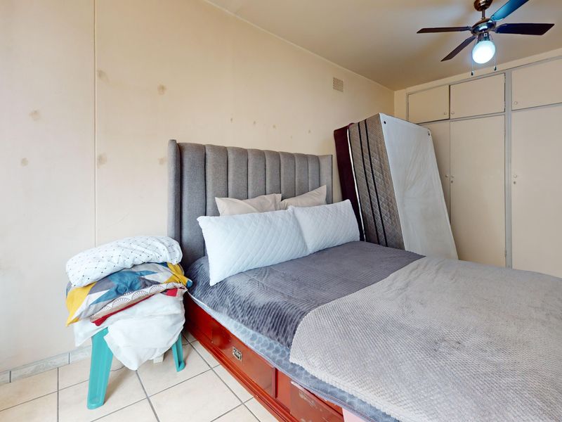 Bedroom featuring built-in cupboards, a ceiling fan, and tiled flooring. The room requires cosmetic attention to the wall surfaces.