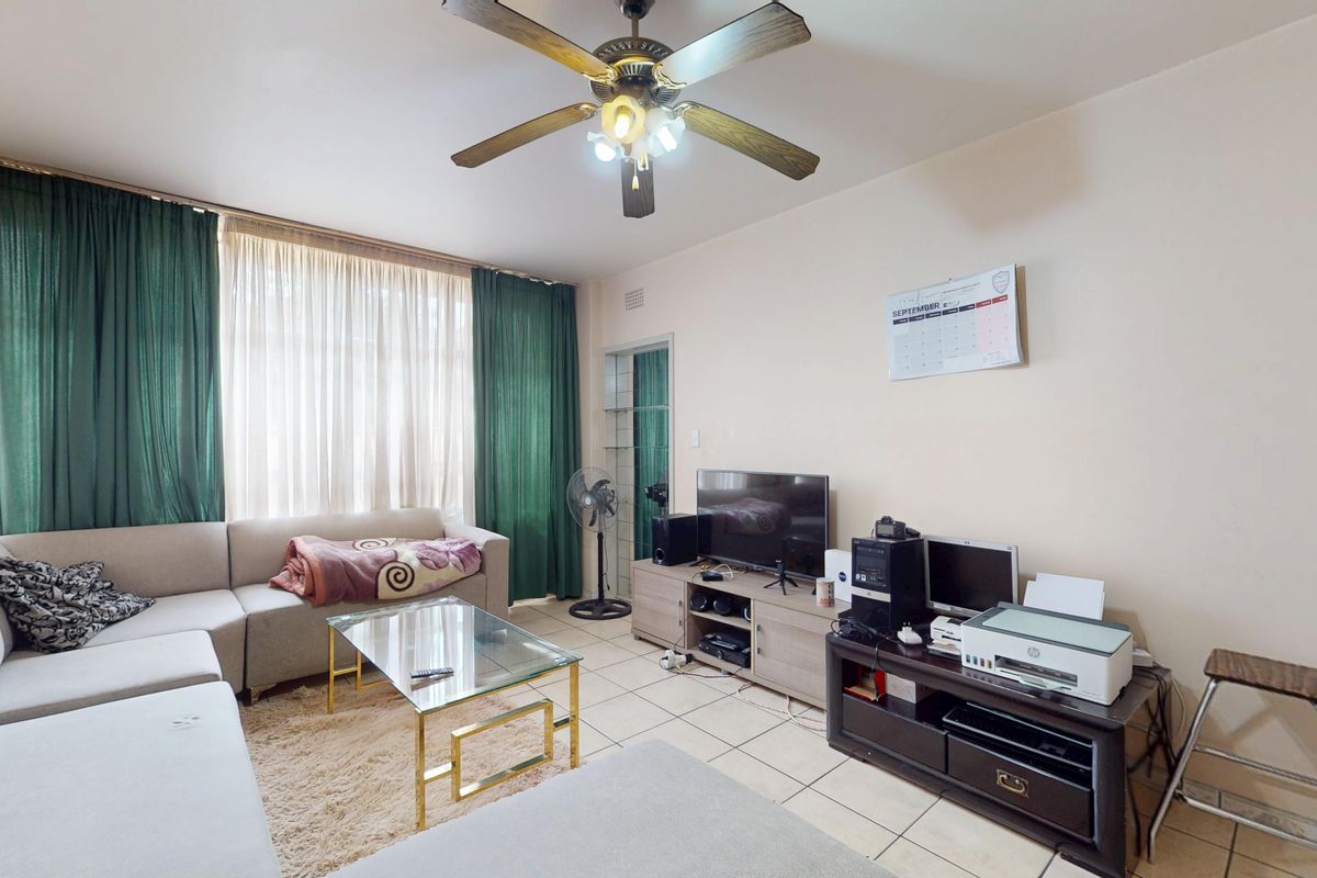 A living room featuring tiled flooring, a ceiling fan, and a large window with floor-to-ceiling curtains.