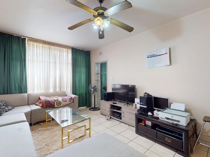 A living room featuring tiled flooring, a ceiling fan, and a large window with floor-to-ceiling curtains.