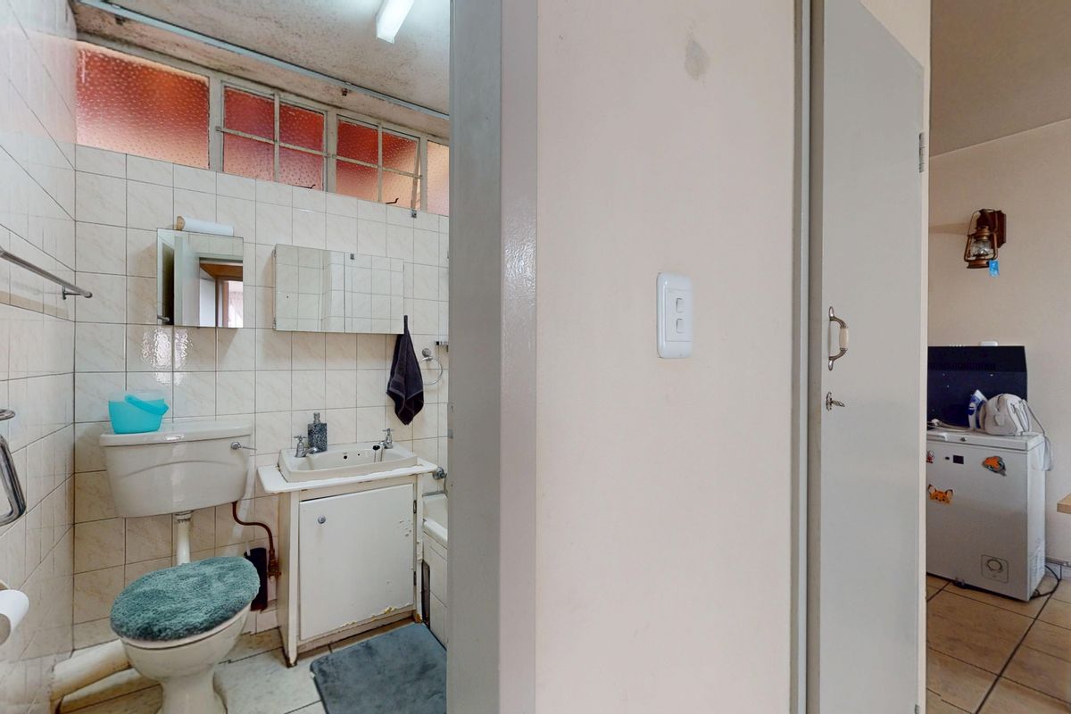 A dated bathroom featuring tiled walls, a vanity basin, and a toilet, requiring modernization to improve its overall condition and aesthetic appeal.