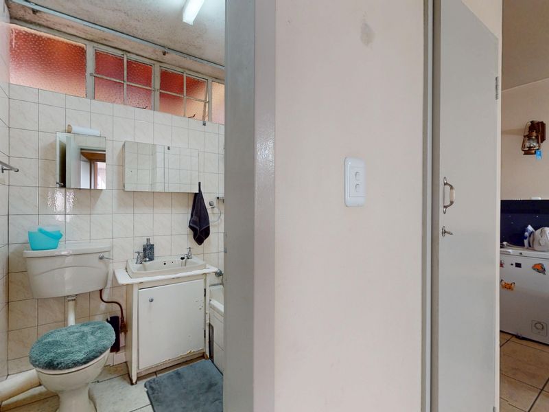 A dated bathroom featuring tiled walls, a vanity basin, and a toilet, requiring modernization to improve its overall condition and aesthetic appeal.
