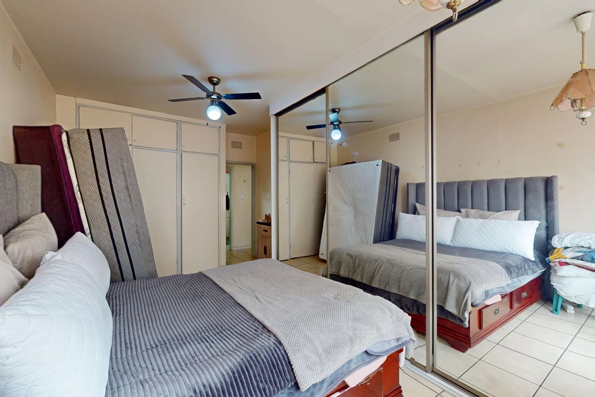 A bedroom featuring built-in cupboards with mirrored sliding doors, a ceiling fan, and tiled flooring. The space requires cosmetic updates to improve its overall condition.