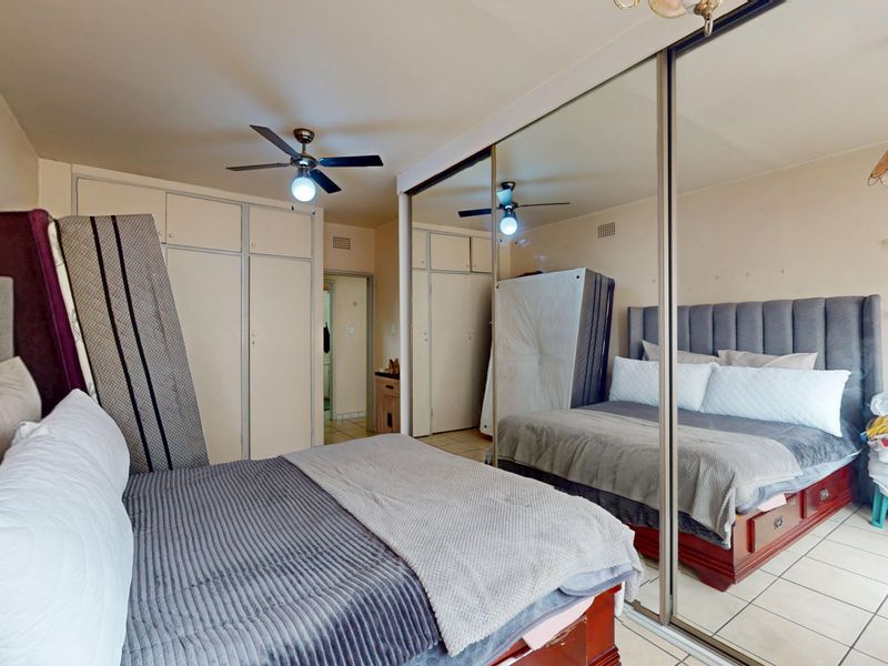 A bedroom featuring built-in cupboards with mirrored sliding doors, a ceiling fan, and tiled flooring. The space requires cosmetic updates to improve its overall condition.