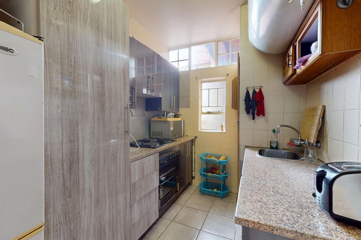 A functional galley-style kitchen featuring granite countertops, built-in cabinetry, an integrated oven and hob, and tiled finishes throughout.