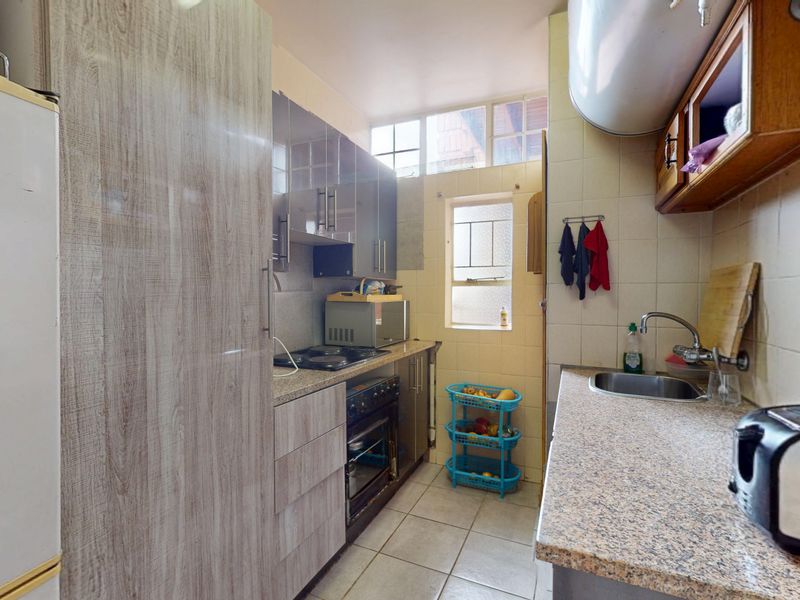 A functional galley-style kitchen featuring granite countertops, built-in cabinetry, an integrated oven and hob, and tiled finishes throughout.