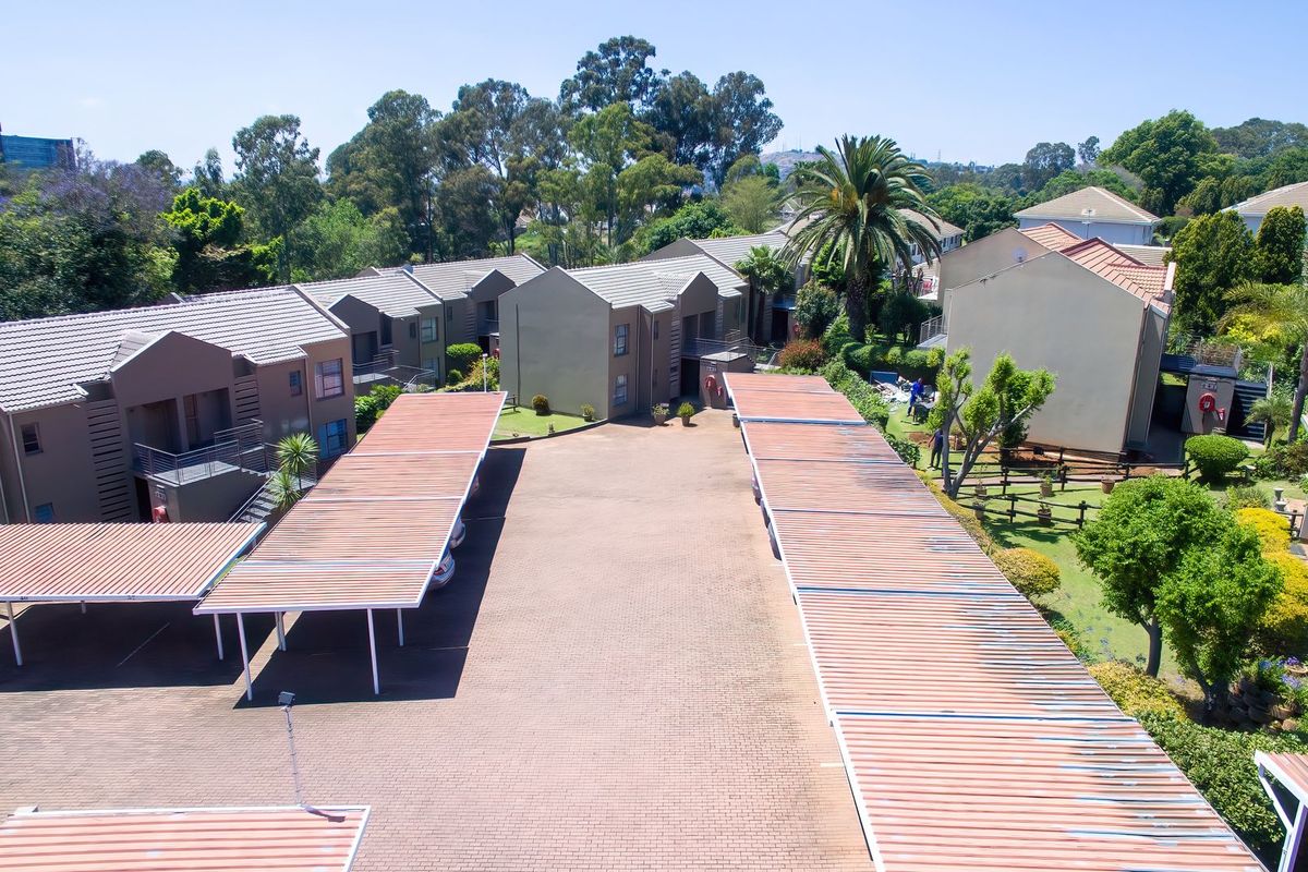 Aerial view of a residential complex featuring multiple townhouse units, paved driveway areas, and covered carport parking structures set within a landscaped environment.